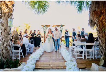 Bride walking a petal-lined aisle across the bridge toward the pavilion