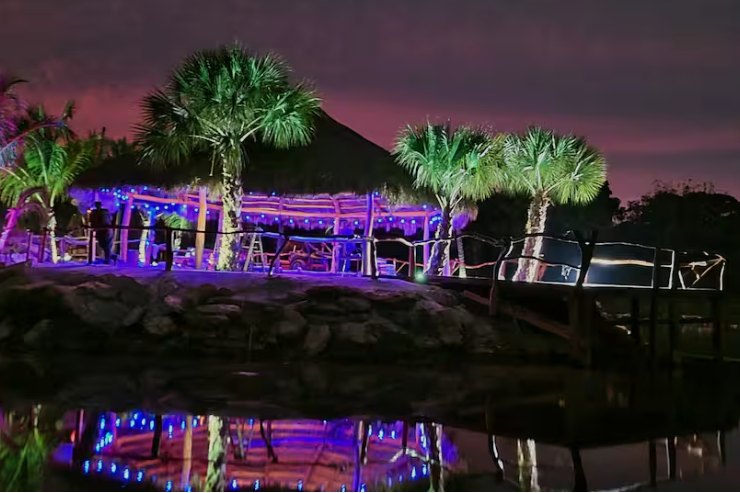 The island pavilion lit in purple and blue at dusk, reflected in the lagoon